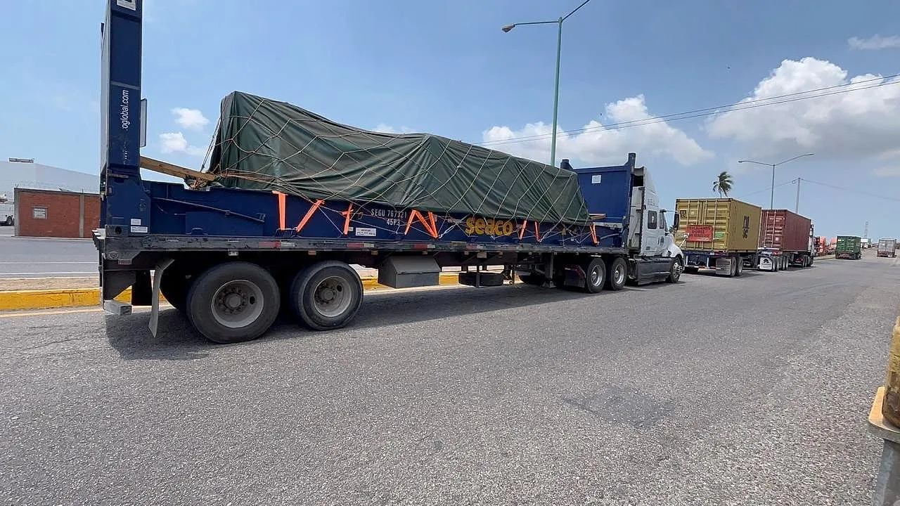 Plataforma con carga encarpada y asegurada, formada en la fila de acceso al puerto.