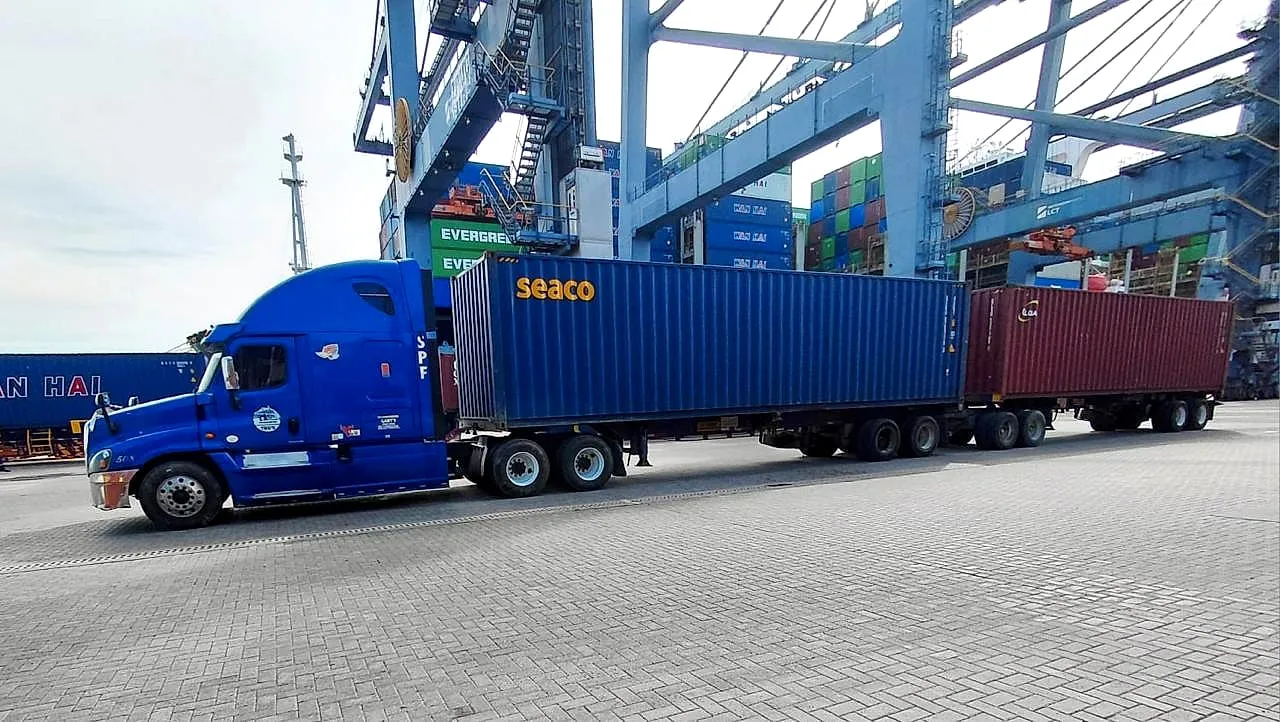 Tractocamión azul de Transportes Gaby's con dos contenedores en full bajo las grúas del puerto.